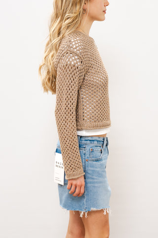 Woman wearing a beige knitted sweater and denim shorts on a white 