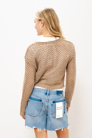 Woman wearing a beige knitted sweater and denim shorts on a white 