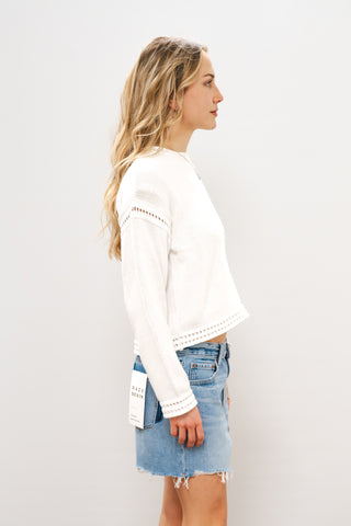 Woman wearing a white blouse with lace details and denim shorts on a plain background