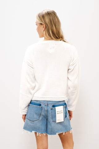 Person wearing a white sweater and denim shorts on a plain background
