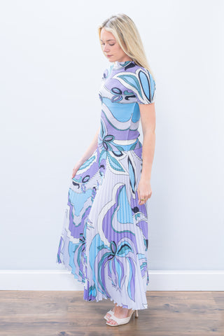Woman wearing a patterned dress standing against a white wall.