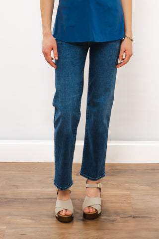 Person wearing blue jeans and beige sandals on a wooden floor with a white wall background