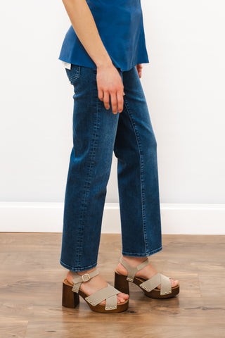 Person wearing blue jeans and beige sandals on a wooden floor with a white wall background