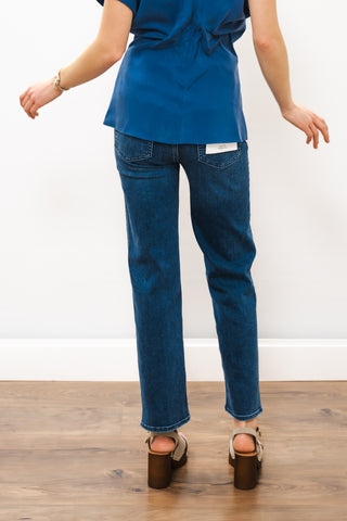 Person wearing blue scrubs and jeans on a wooden floor with a white wall background