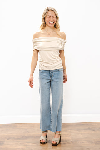 Woman wearing a beige off-shoulder top and light blue jeans on a white background