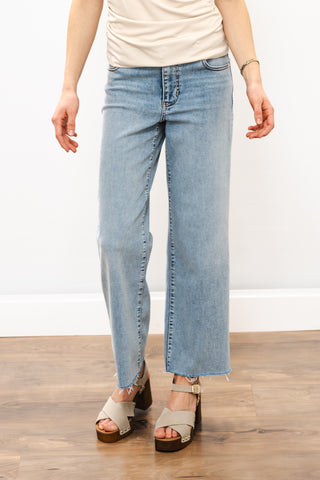 a person wearing light blue jeans and heels on a wooden floor against a blank wall