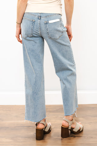 Light blue jeans worn by a person on a wooden floor with a white wall background