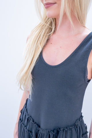 Person wearing a dark gray sleeveless top with ruffled trim on a plain background