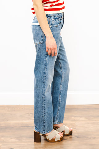 Person wearing blue jeans and a red and white striped shirt on a wooden floor.