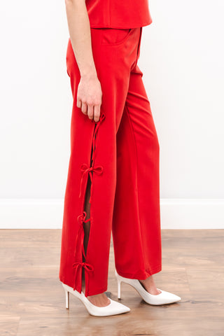 Person wearing a red outfit with wide-leg pants and white shoes on a wooden floor.