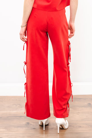 Red jumpsuit with side tie details on a wooden floor.