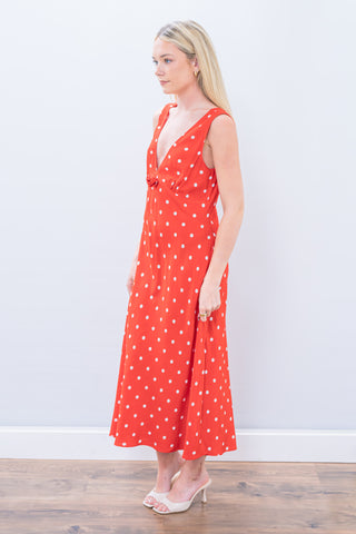 Woman wearing a red polka dot dress against a white wall.
