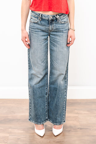 Person wearing blue jeans and a red top on a wooden floor with a white wall background