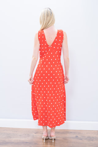 Woman wearing a red polka dot dress against a white wall.