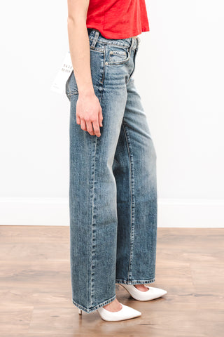 Person wearing blue jeans and a red top on a wooden floor.