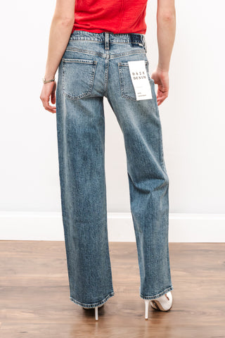 Person wearing blue jeans with a visible brand label on a plain background