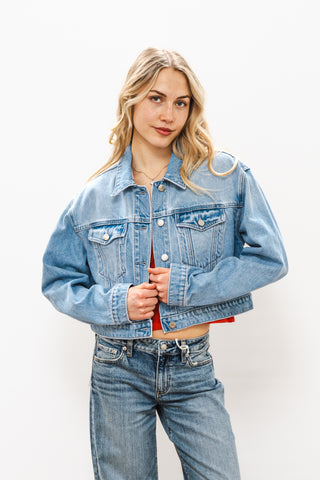Woman wearing a light blue denim jacket and jeans on a white background