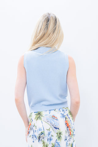 Woman wearing a light blue sleeveless sweater over a colorful skirt on a white background