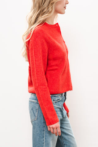 a blonde woman in a red sweater and blue jeans standing against a blank wall