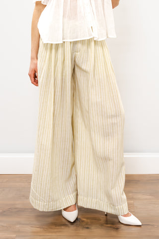 Person wearing light-colored striped pants and a white top on a wooden floor with a white wall background.
