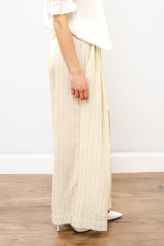 Person wearing a white top and beige pleated skirt on a wooden floor with a white wall background