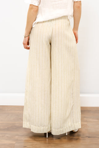 Person wearing beige wide-leg pants on a wooden floor with a white wall background
