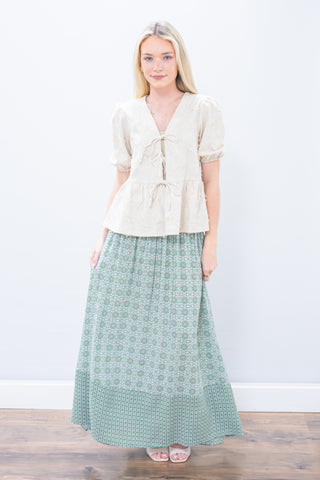 Woman wearing a white blouse and green patterned skirt on a plain background