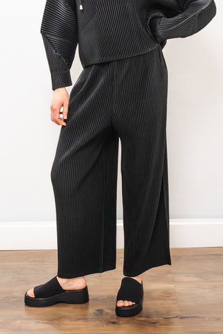 Person wearing a black ribbed outfit with wide-leg pants on a wooden floor.