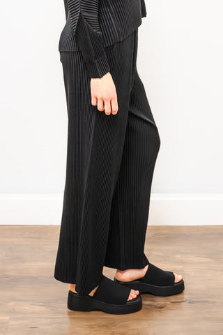 Person wearing a black outfit with wide-leg pants on a wooden floor.