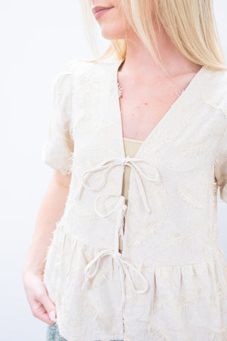 Close-up of a person wearing a light-colored sleeveless top with a tie detail on a plain background