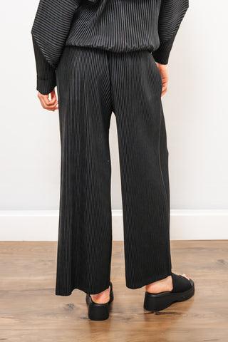 Person wearing black pinstripe pants and a matching top on a wooden floor.