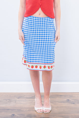 Person wearing a blue gingham skirt with strawberry pattern on a wooden floor.