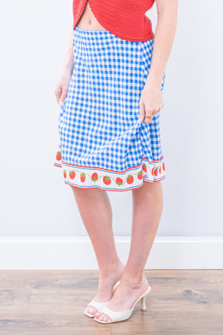 Person wearing a blue gingham skirt with strawberry pattern on a white background