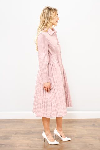 Woman wearing a pink ribbed dress standing against a white wall.