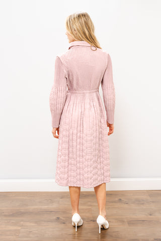 Woman wearing a pink ribbed dress standing on a wooden floor with a white wall background
