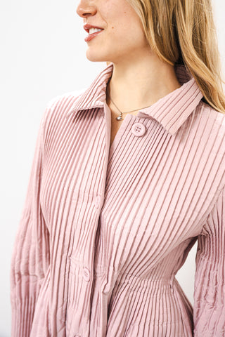 Close-up of a person wearing a pink ribbed shirt against a white background
