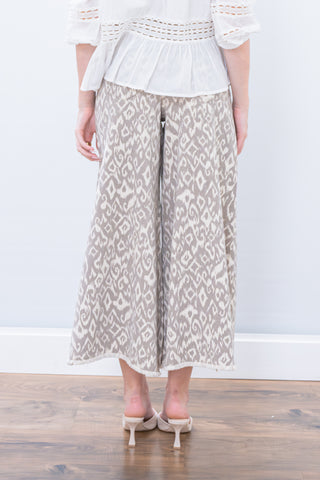 Person wearing a white top and patterned skirt on a wooden floor with a white wall background
