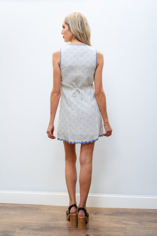 Woman wearing a light-colored dress with a subtle pattern against a plain white wall.