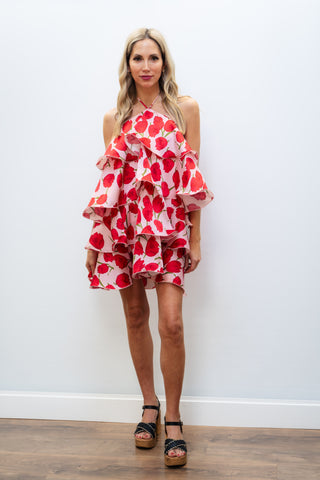 Woman wearing a red and white floral dress against a white wall.