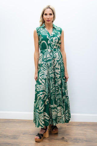 Woman wearing a green and white patterned sleeveless dress against a white wall.
