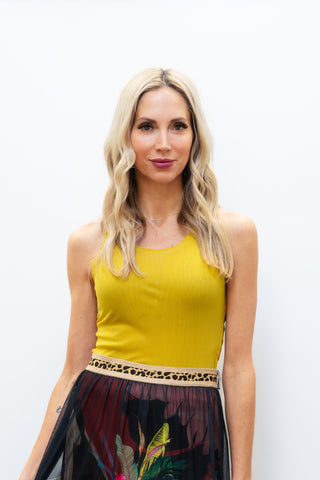 Woman wearing a yellow top and floral sheer skirt against a white wall.