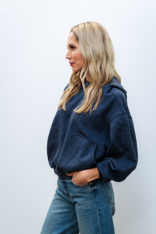 Woman wearing a navy blue hoodie and jeans against a white background